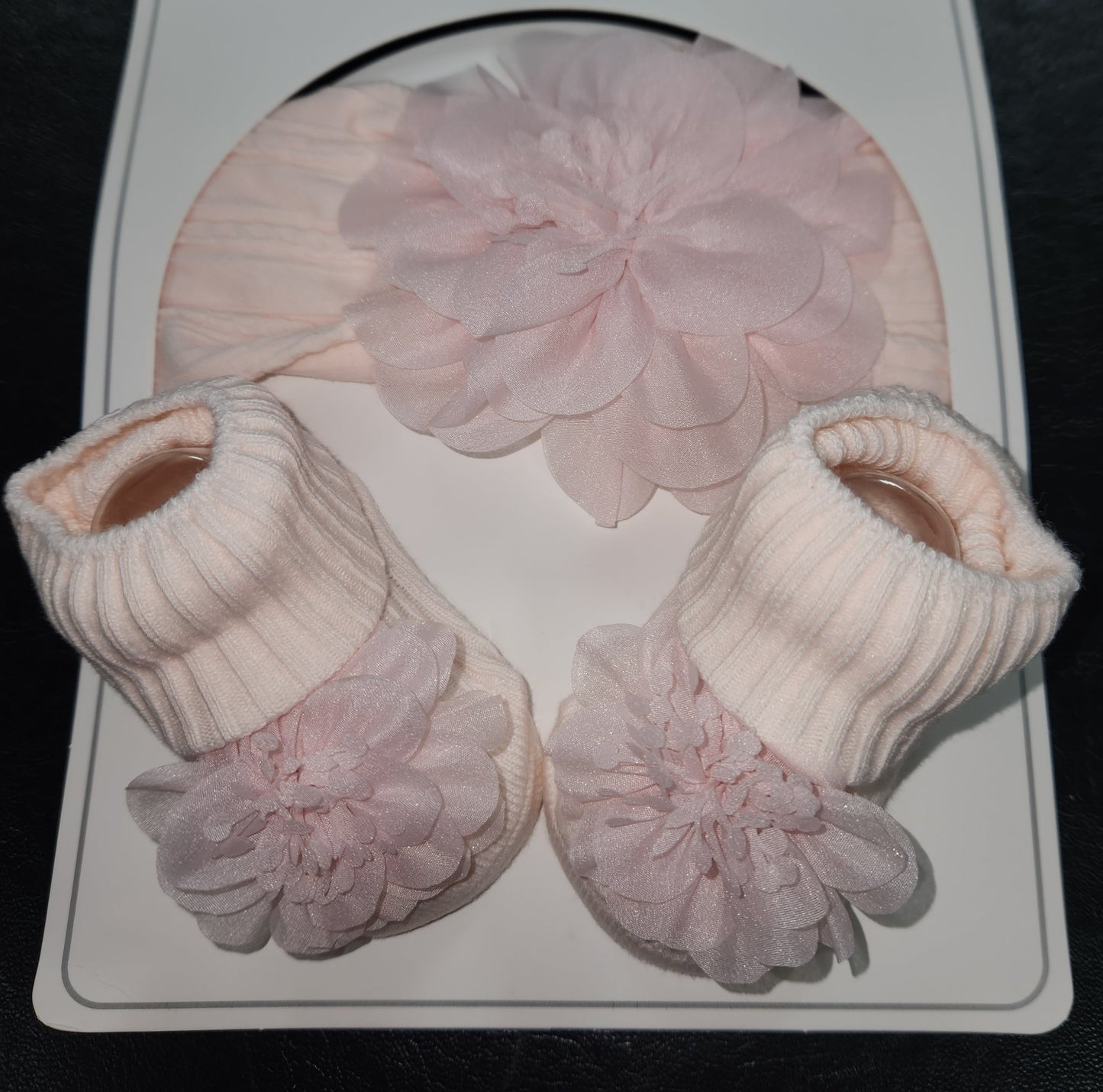 Set of pink baby booties with ruffled tops on a white card.